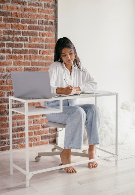 Woman working at desk with laptop and papers in natural light
